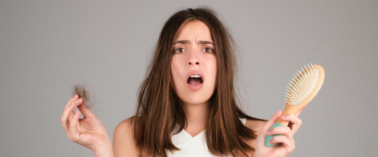 Devojka drzi cetku u jednoj ruci i kosu u drugoj