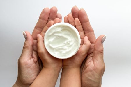 Close up of woman and childs hands holding hand cream on white background. Skincare and moisturizing concept. Design for healthcare, beauty, wellness, and family care poster. High quality photo